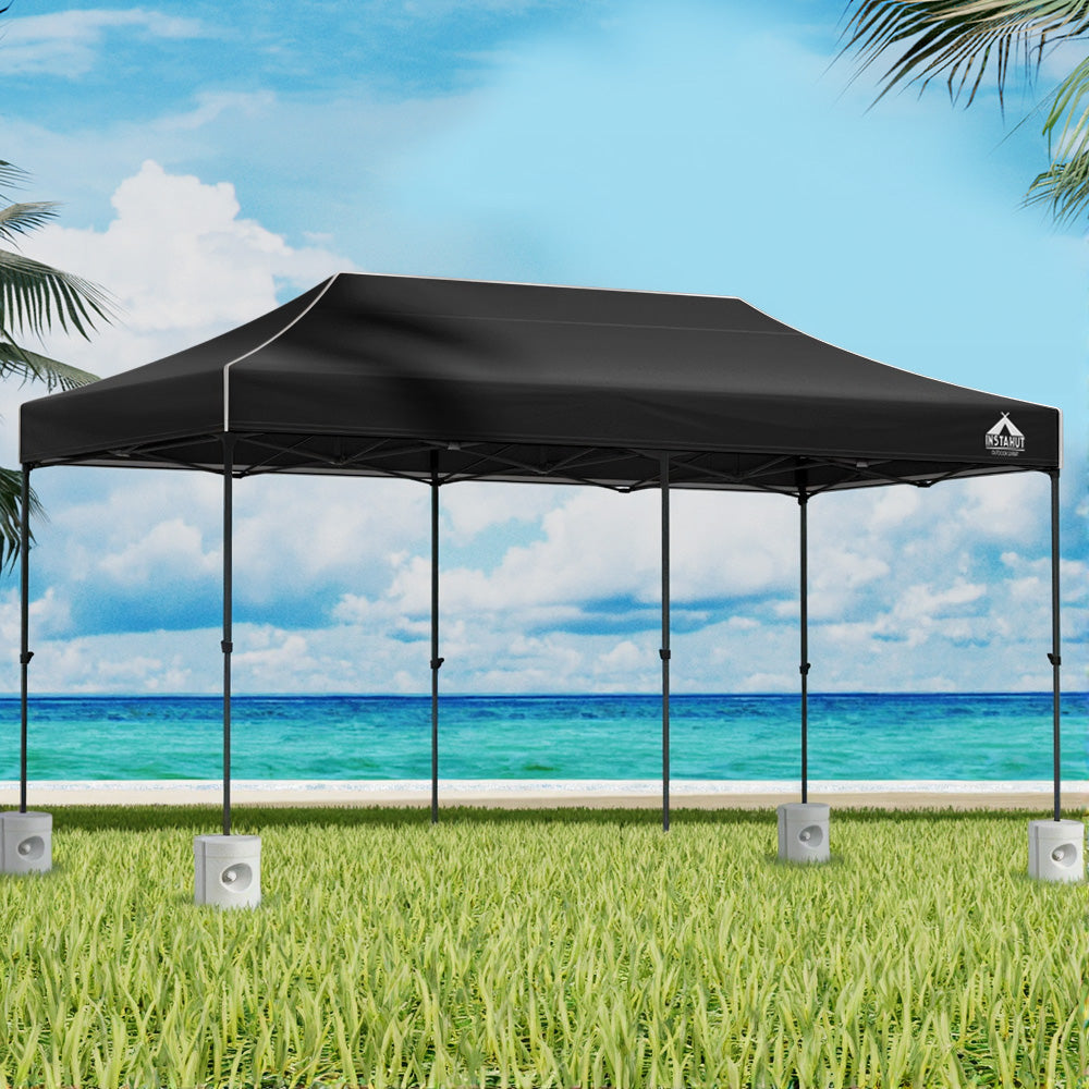 Black 6 x 3 m pop up gazebo set up outdoors with white base pods on the legs