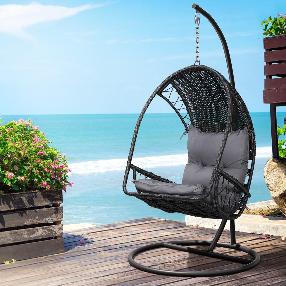 Gerroa black resin wicker hanging egg chair with stand on a patio
