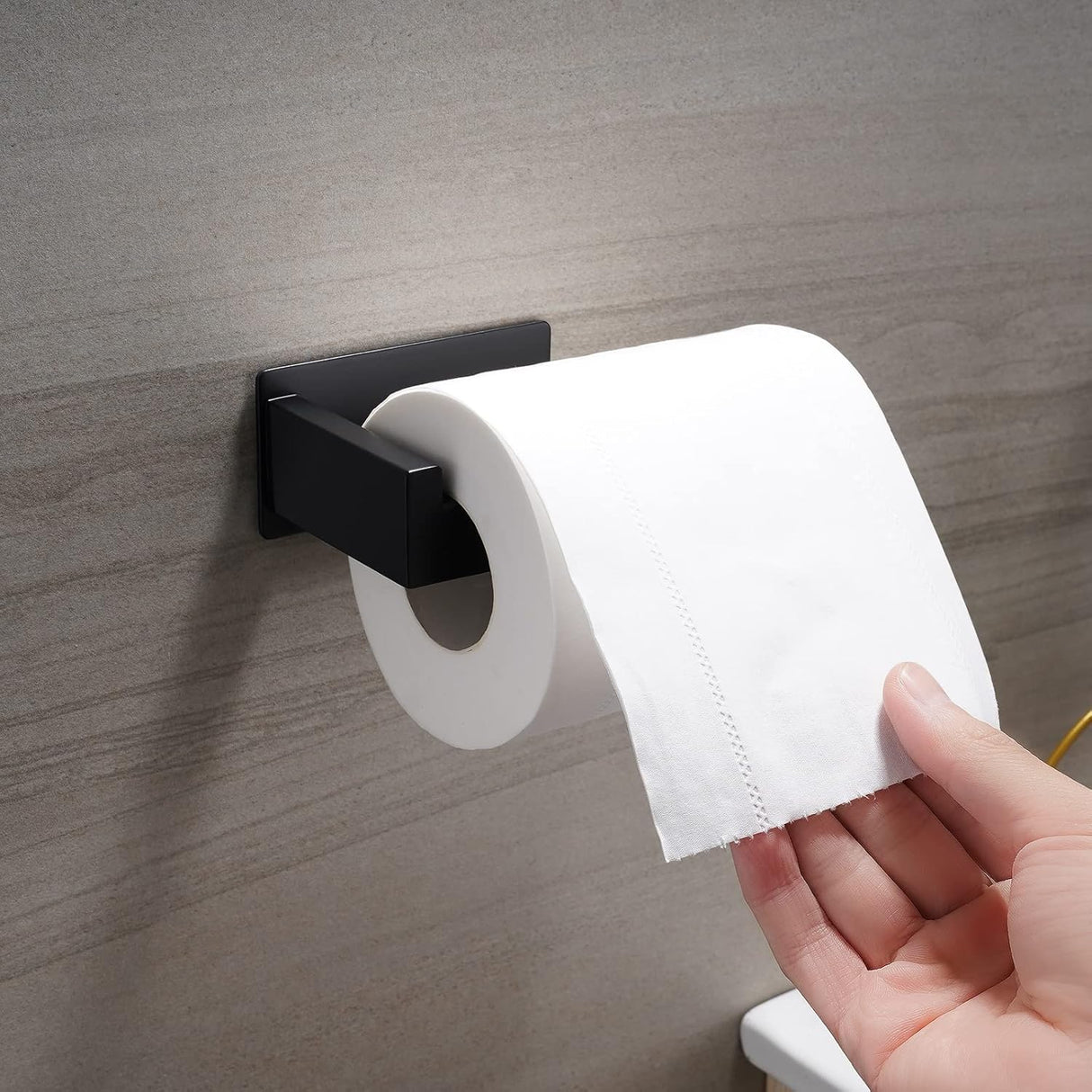 Black adhesive roll holder mounted on a smooth tiled bathroom wall