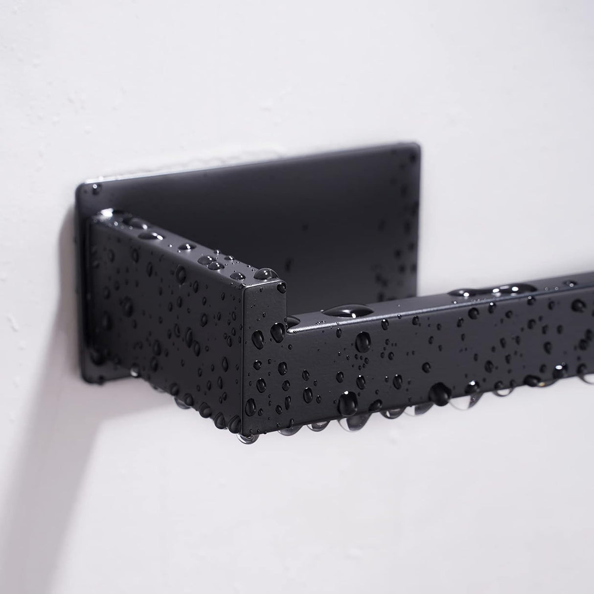 Black toilet roll holder loaded with a paper roll on a tiled bathroom wall