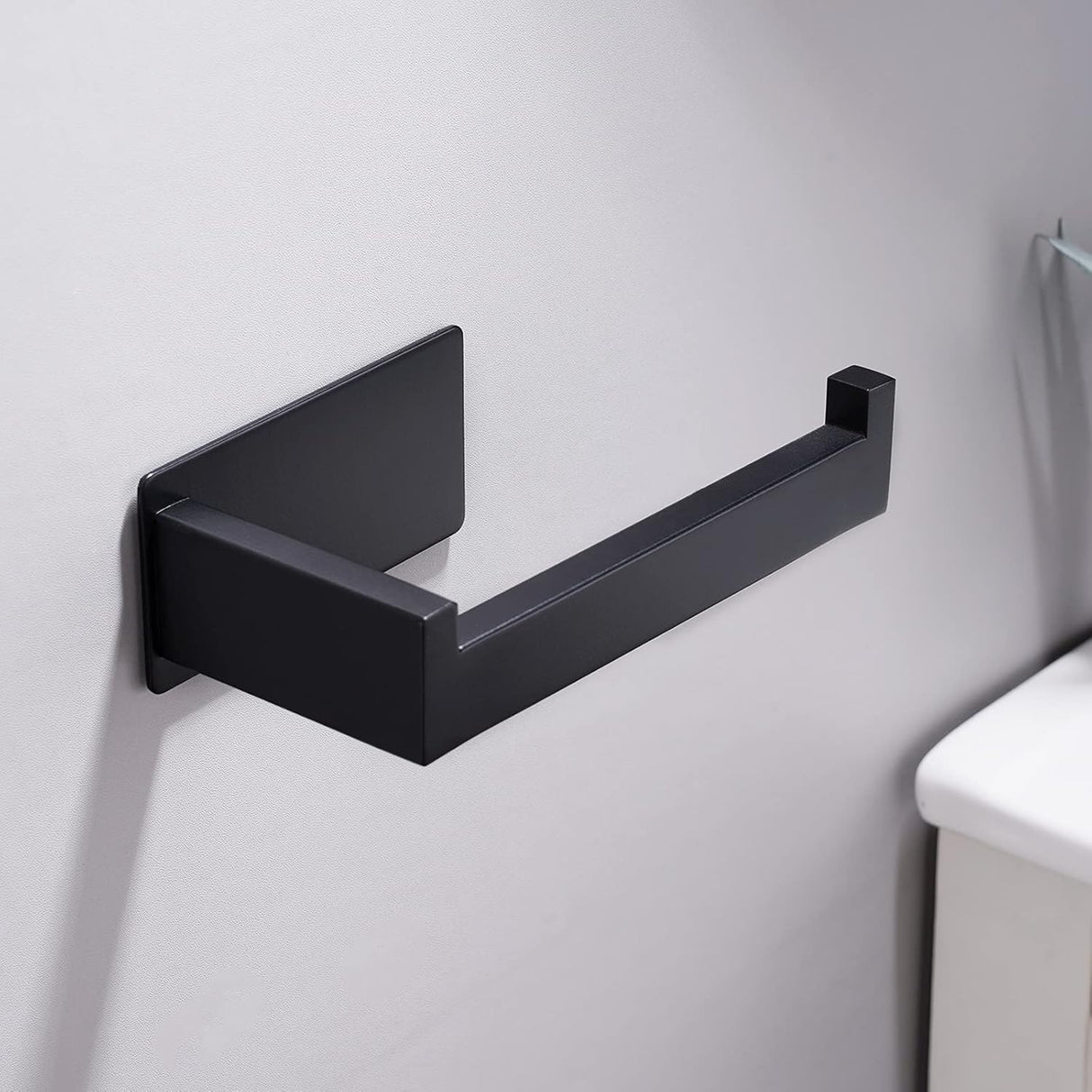 Black adhesive toilet roll holder installed beside a toilet in a modern bathroom
