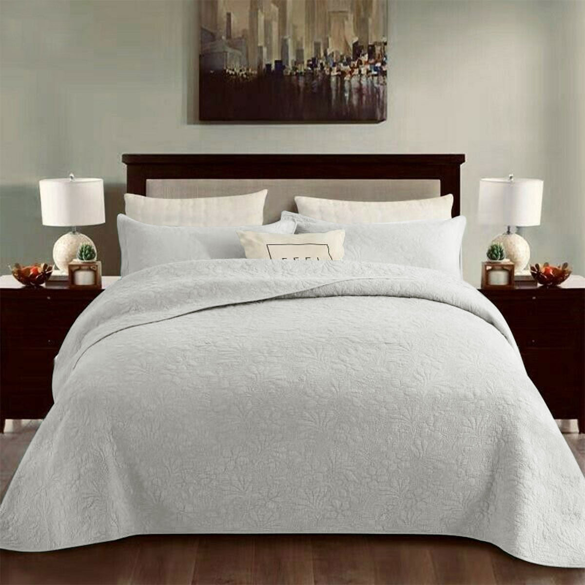 White cotton coverlet set with a tonal floral quilting and two pillow shams on a queen bed