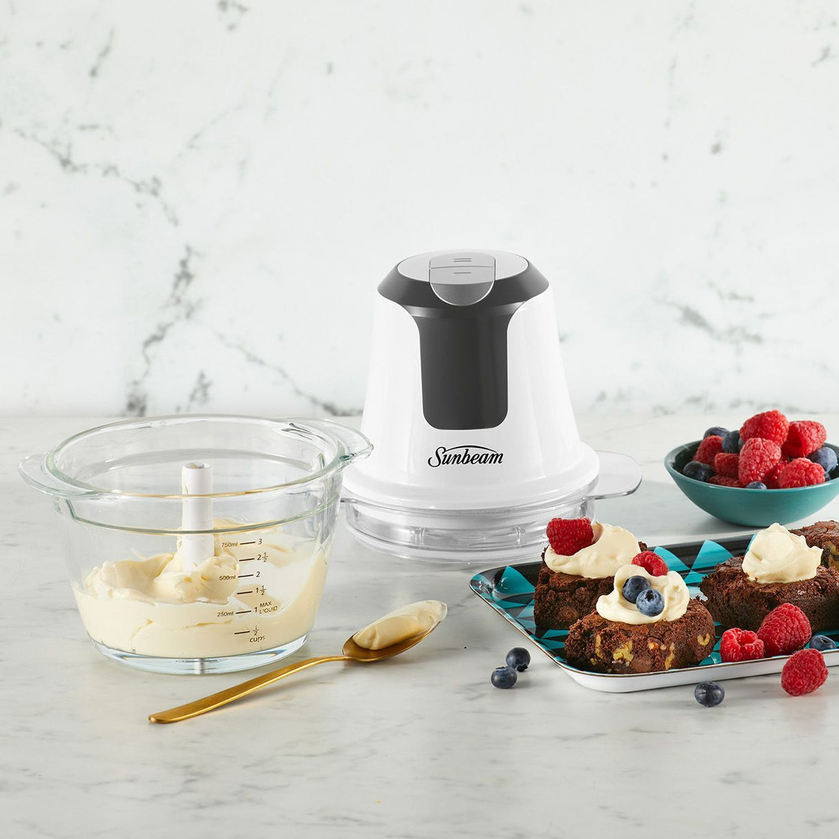 Mini food chopper on a bench with chopped herbs in the glass bowl