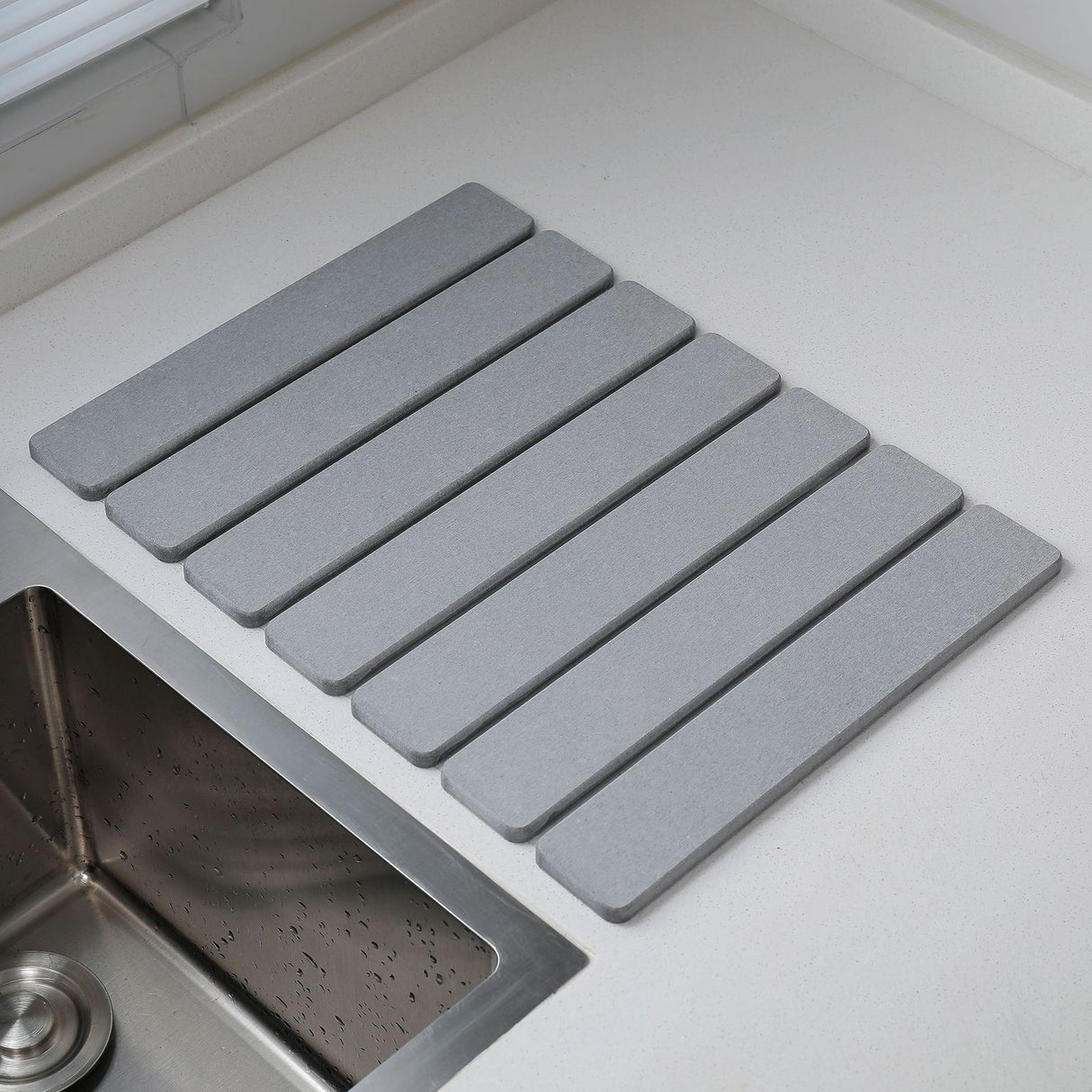 Light grey folding diatomaceous earth drain mat laid flat beside a sink
