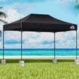 Black 4.5 x 3 m pop up gazebo set up outdoors with white base pods on the legs