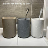 Bathroom tumblers holding toothbrushes and a tube of toothpaste beside a basin