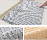 Beige braided bath mat placed beside a bath on a tiled bathroom floor