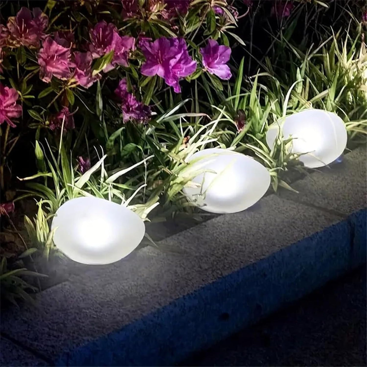 Solar cobblestone shaped garden light glowing in a flower bed