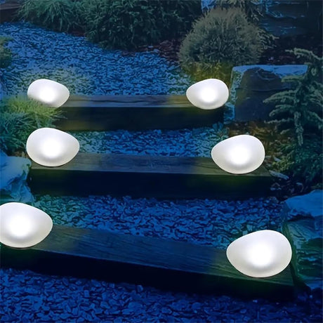 Solar cobblestone shaped garden light glowing in a flower bed