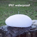 Solar cobblestone shaped garden light glowing in a flower bed