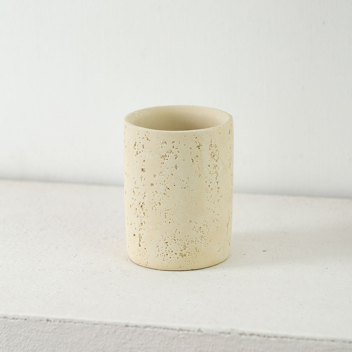 Sandstone toothbrush holder cup holding toothbrushes beside a basin
