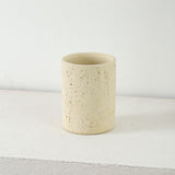 Sandstone toothbrush holder cup holding toothbrushes beside a basin