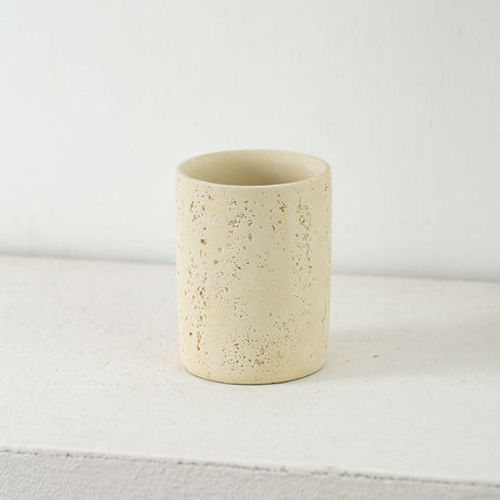 Sandstone toothbrush holder cup holding toothbrushes beside a basin