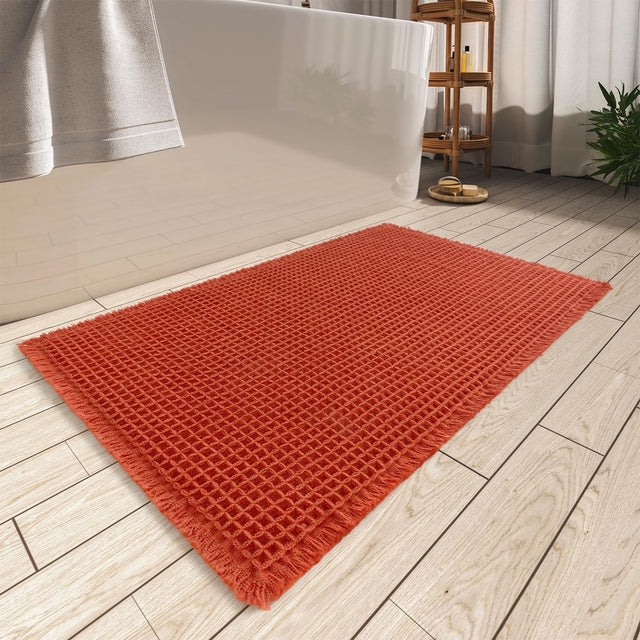 Orange waffle bath mat with tassels, 46 x 76 cm, on a bathroom floor