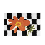 Orange flower checkered doormat laid flat, showing the black and white grid pattern and soft pile