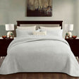 White cotton coverlet set with a tonal floral quilting and two pillow shams on a queen bed