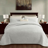 White cotton coverlet set with a tonal floral quilting and two pillow shams on a queen bed