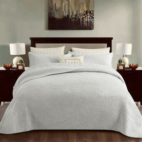 White cotton coverlet set with a tonal floral quilting and two pillow shams on a queen bed