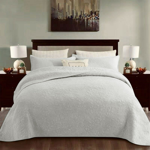 White cotton coverlet set with a tonal floral quilting and two pillow shams on a queen bed
