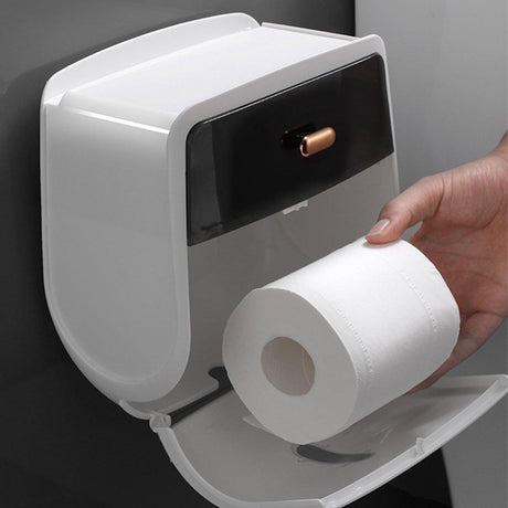 Grey enclosed toilet roll holder mounted on a bathroom wall beside a toilet