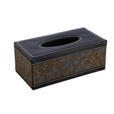 Black tissue box holder on a desk with tissue drawn through the top