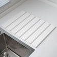 White folding diatomaceous earth drain mat laid flat beside a sink