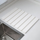 White folding diatomaceous earth drain mat laid flat beside a sink