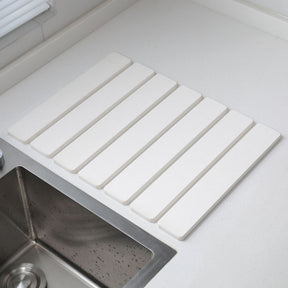 White folding diatomaceous earth drain mat laid flat beside a sink