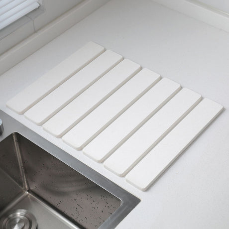 White folding diatomaceous earth drain mat laid flat beside a sink