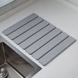 Light grey folding diatomaceous earth drain mat laid flat beside a sink