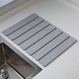 Light grey folding diatomaceous earth drain mat laid flat beside a sink