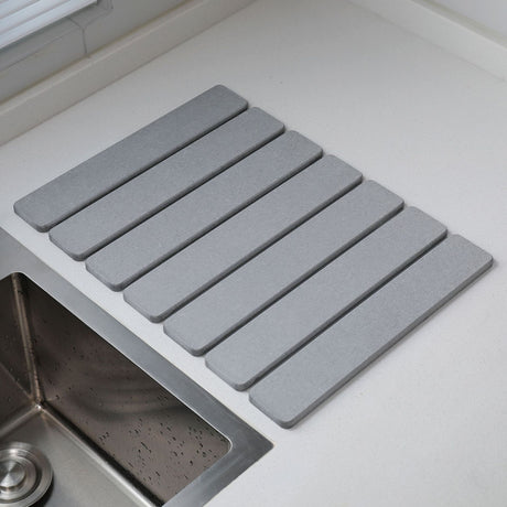 Light grey folding diatomaceous earth drain mat laid flat beside a sink