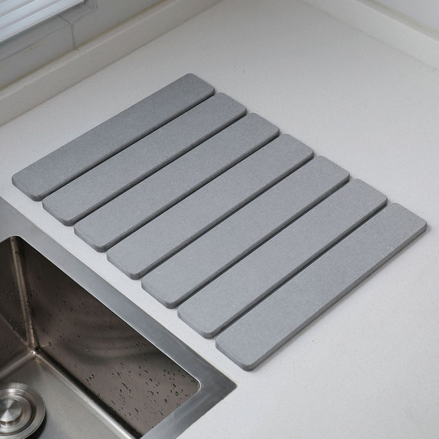Light grey folding diatomaceous earth drain mat laid flat beside a sink