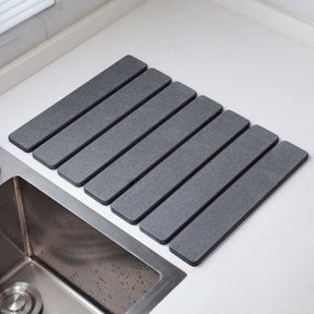 Dark grey folding diatomaceous earth drain mat laid flat beside a sink