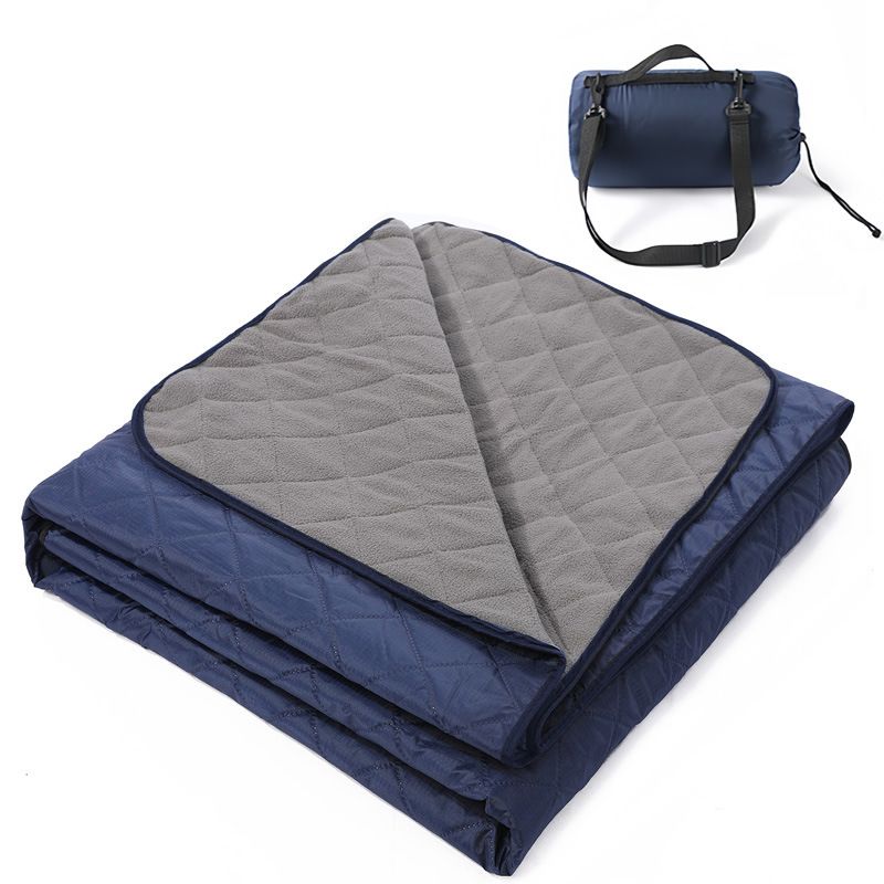 Grasmere double layer fleece picnic blanket in navy blue folded beside its zippered shoulder carry bag on grass